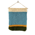 Crocheted wall hanging with blue, beige, and green stripes on a white background
